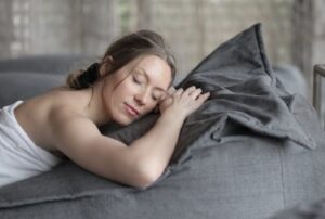 Peaceful woman with closed eyes sleeping on a cozy gray couch, wrapped in a towel indoors.