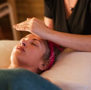 Relaxed woman with closed eyes lying under blanket while getting reiki therapy treatment from unrecognizable therapist in cozy salon with blurred background
