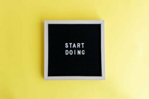 Black message board with 'Start Doing' on a bright yellow background for inspiration.